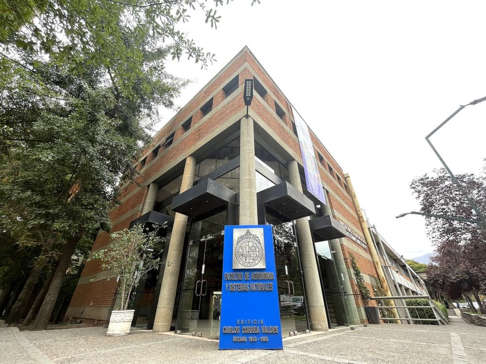 Fotografía del frontis de la Facultad de Agronomía y Sistemas Naturales UC, en frente se ve un cartel con el nombre de la Facultad