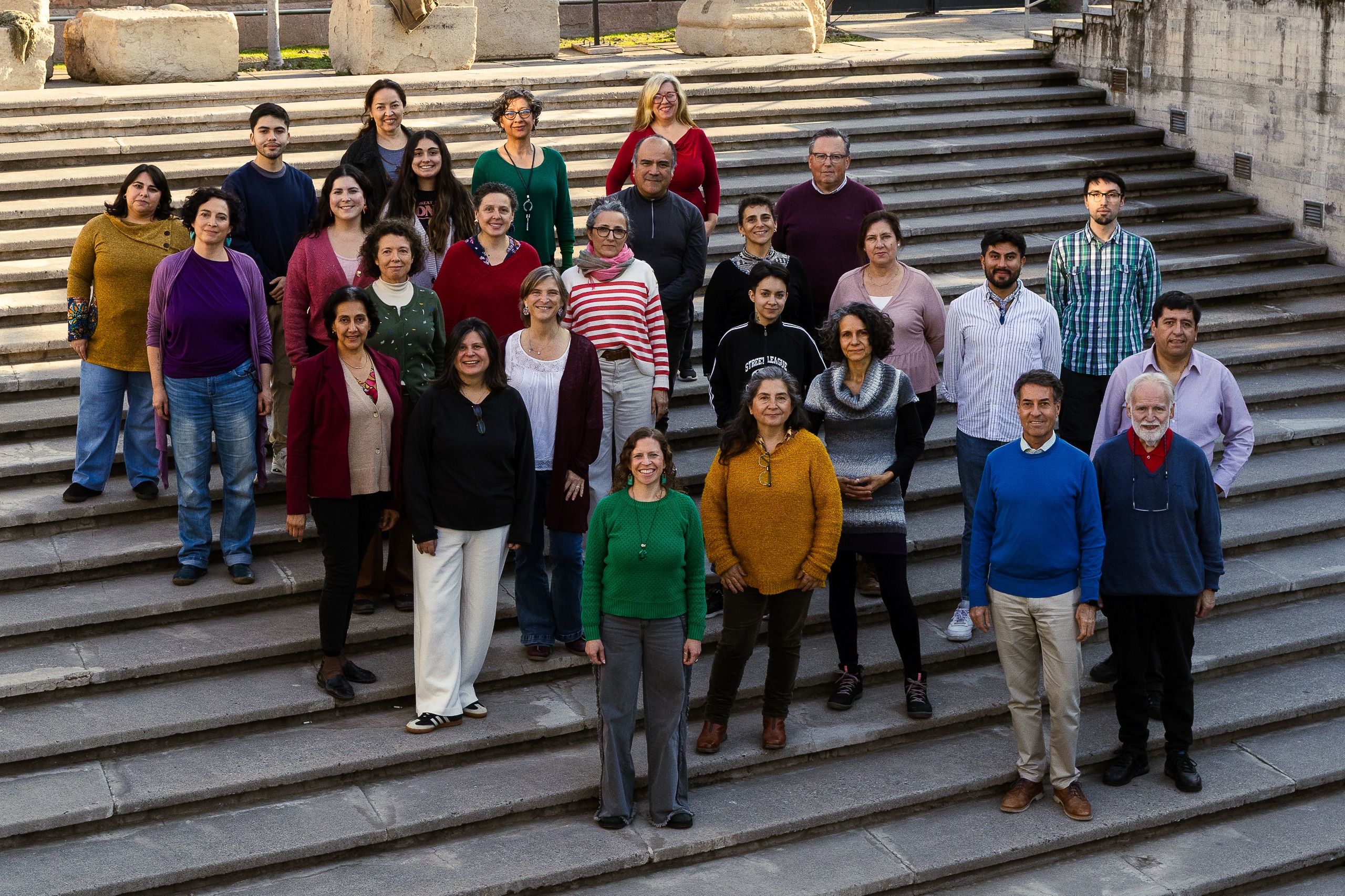 Fotografía de parte de los miembros del Coro Alumni UC vestidos de distintos colores en una gran escalera amplia