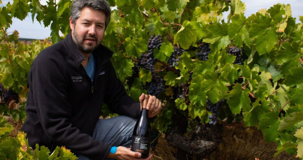 Fotografía del egresado Rafael Urrejola en un viñedo con un botella de vino en mano