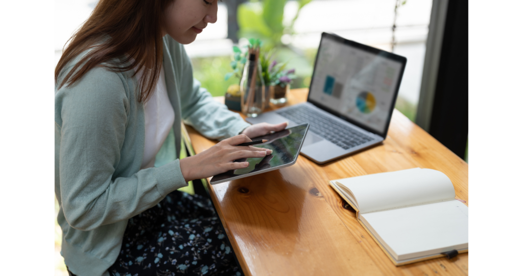 Imagen de una mujer usando una tablet con una laptop de fondo