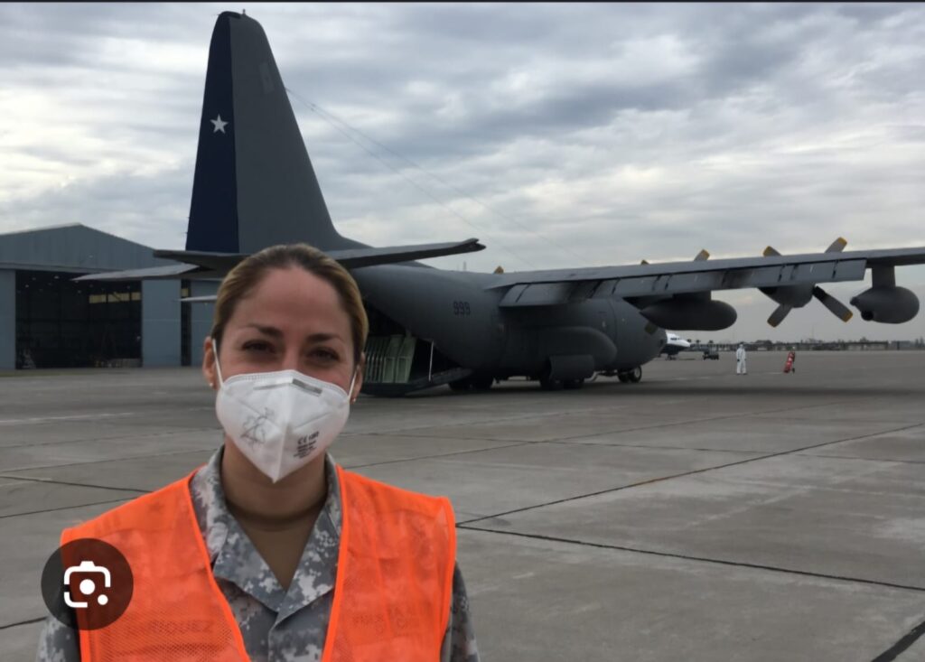 Fotografía de María en una base aérea, frente a un avión estacionado en la pista.
