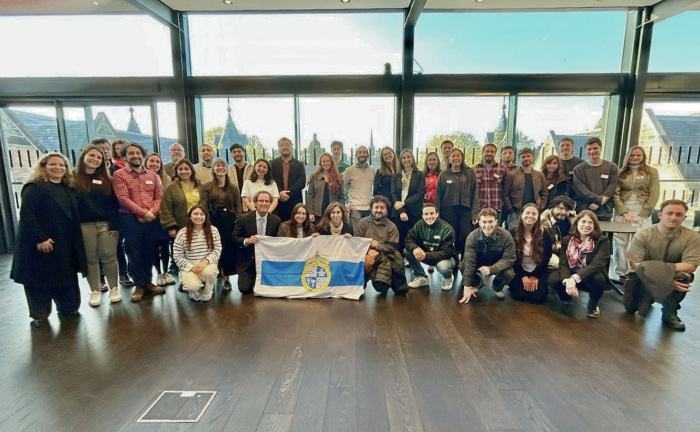 Fotografía de un grupo de más de 30 personas sosteniendo la bandera de la Universidad Católica
